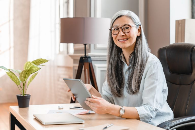 Confident middle-aged businesswoman using tablet at work place in office